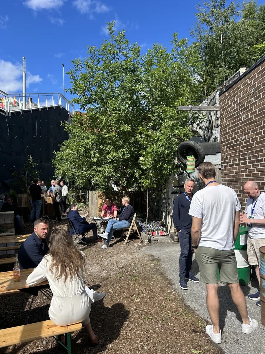 Deltakere snakker sammen rundt bord i et uterom i solskinn.