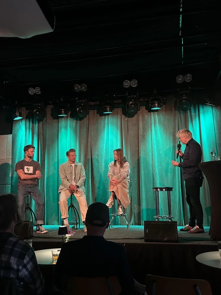 Tre paneldeltakere sitter på scenen mens en samtaleleder står til høyre.